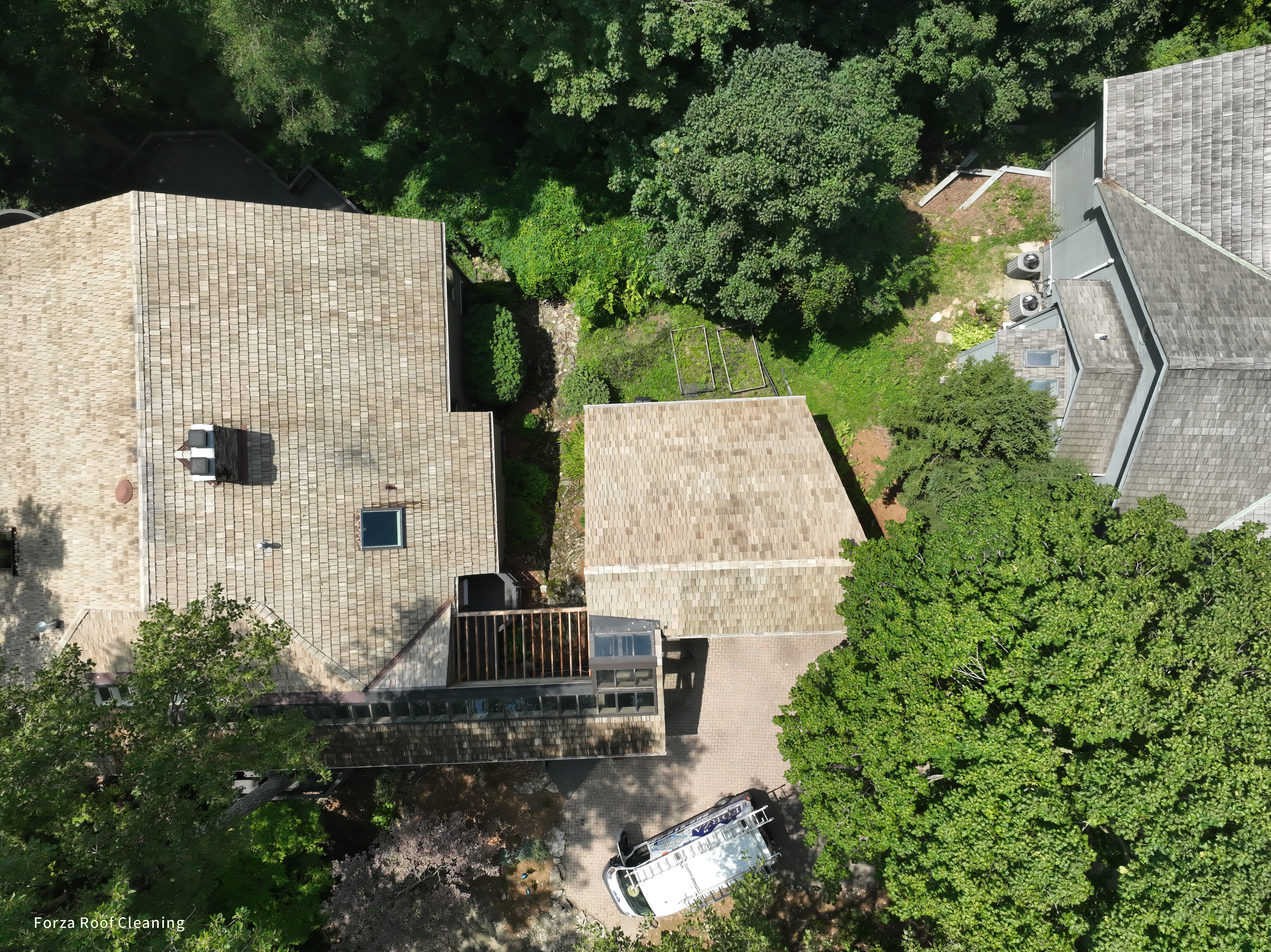 After cedar roof cleaning - overhead view of quarry-side home with golden-tan cedar shakes on main house and outbuilding, neighbor's dark untreated roof visible on right, The Quarry Dublin Ohio