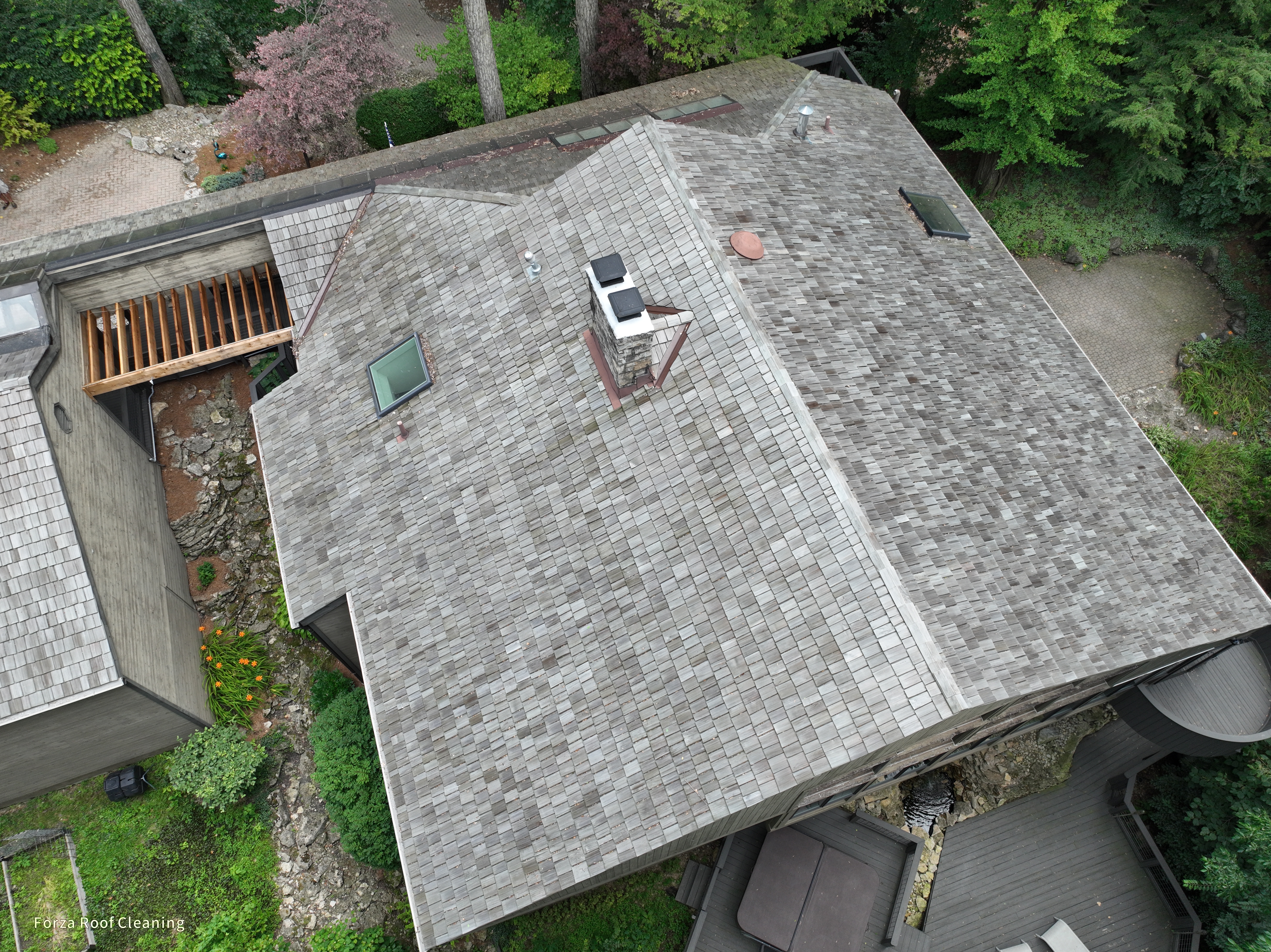 Before cedar roof cleaning - closer overhead showing stone chimney with copper cap, skylight, multiple hips and valleys, dark patchy weathering on cedar shakes, The Quarry Dublin Ohio