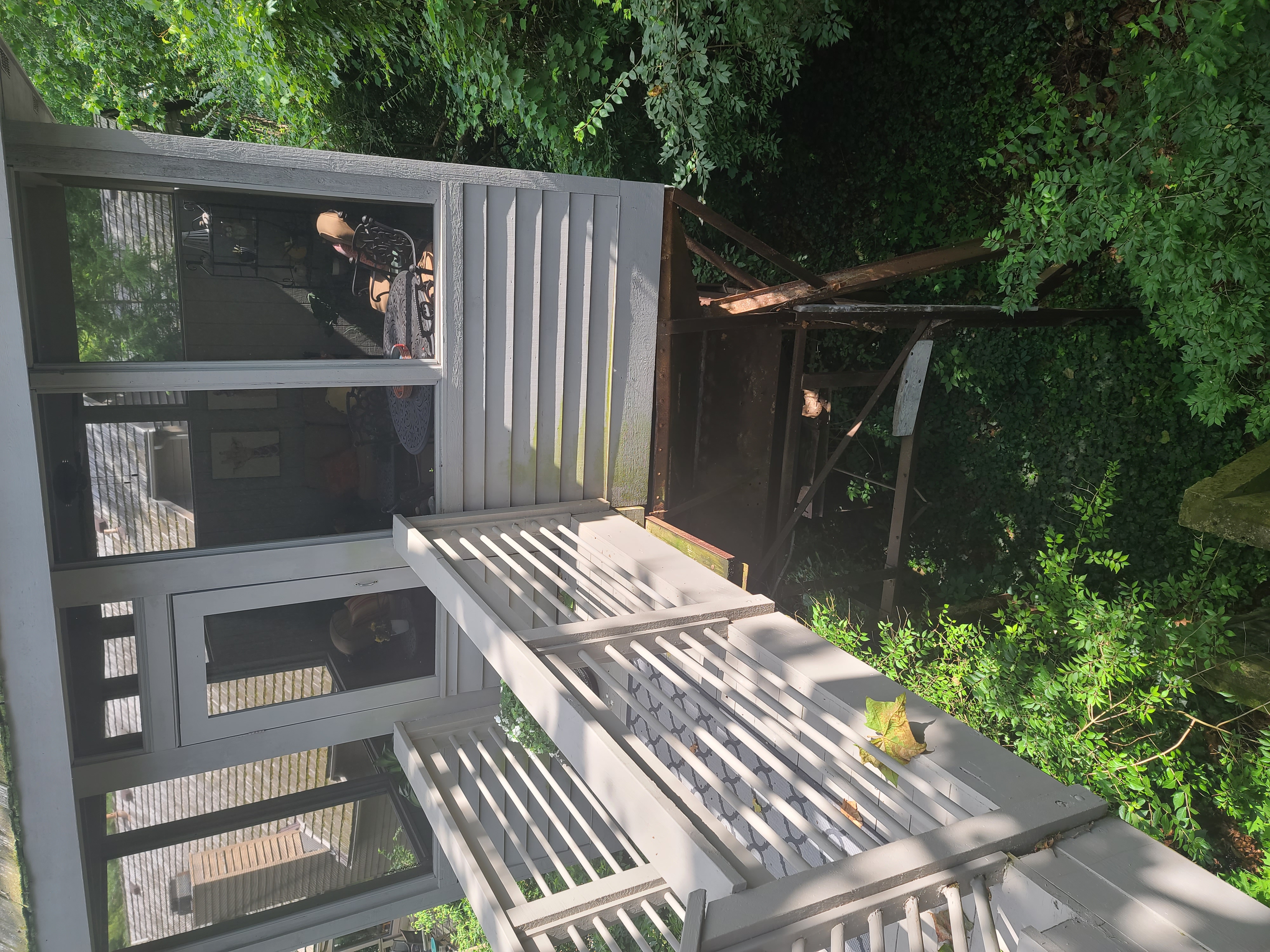 Elevated screened porch on stilts above ravine, metal supports visible below, walkway railing, dense vegetation below, The Quarry Dublin Ohio