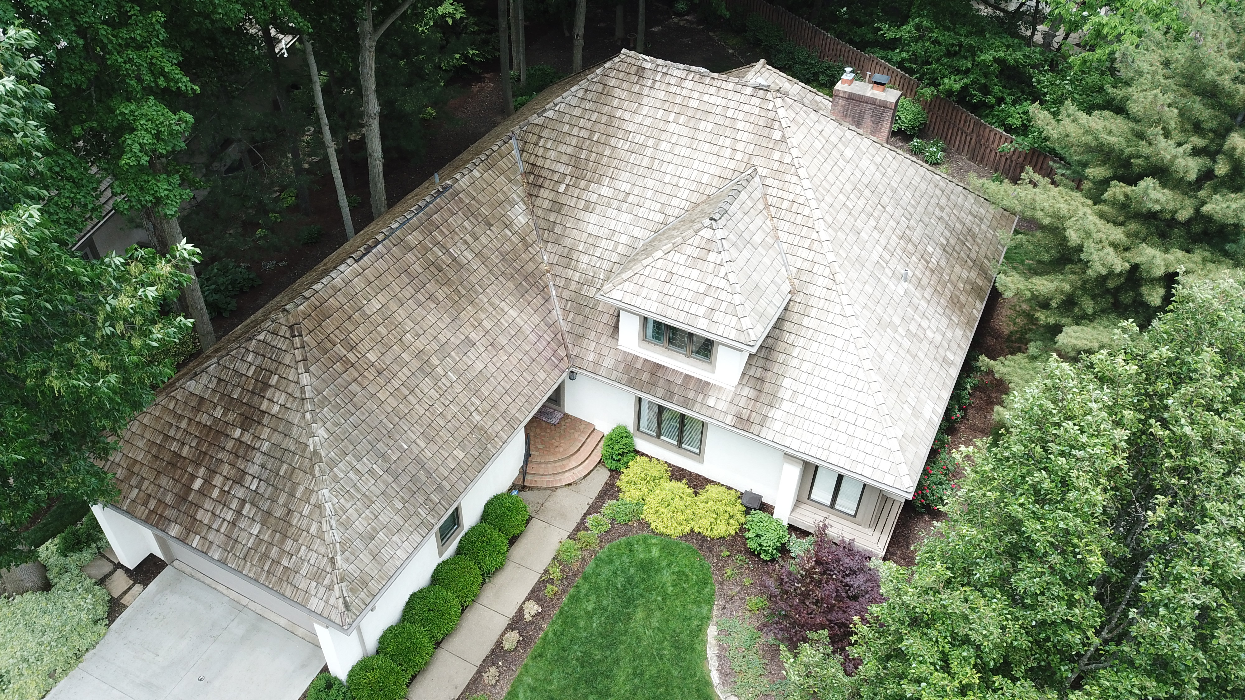 After cedar roof cleaning - full home view showing golden-tan cedar shakes surrounded by dense tree canopy, brick chimney, curved front walkway, The Sanctuary Columbus Ohio