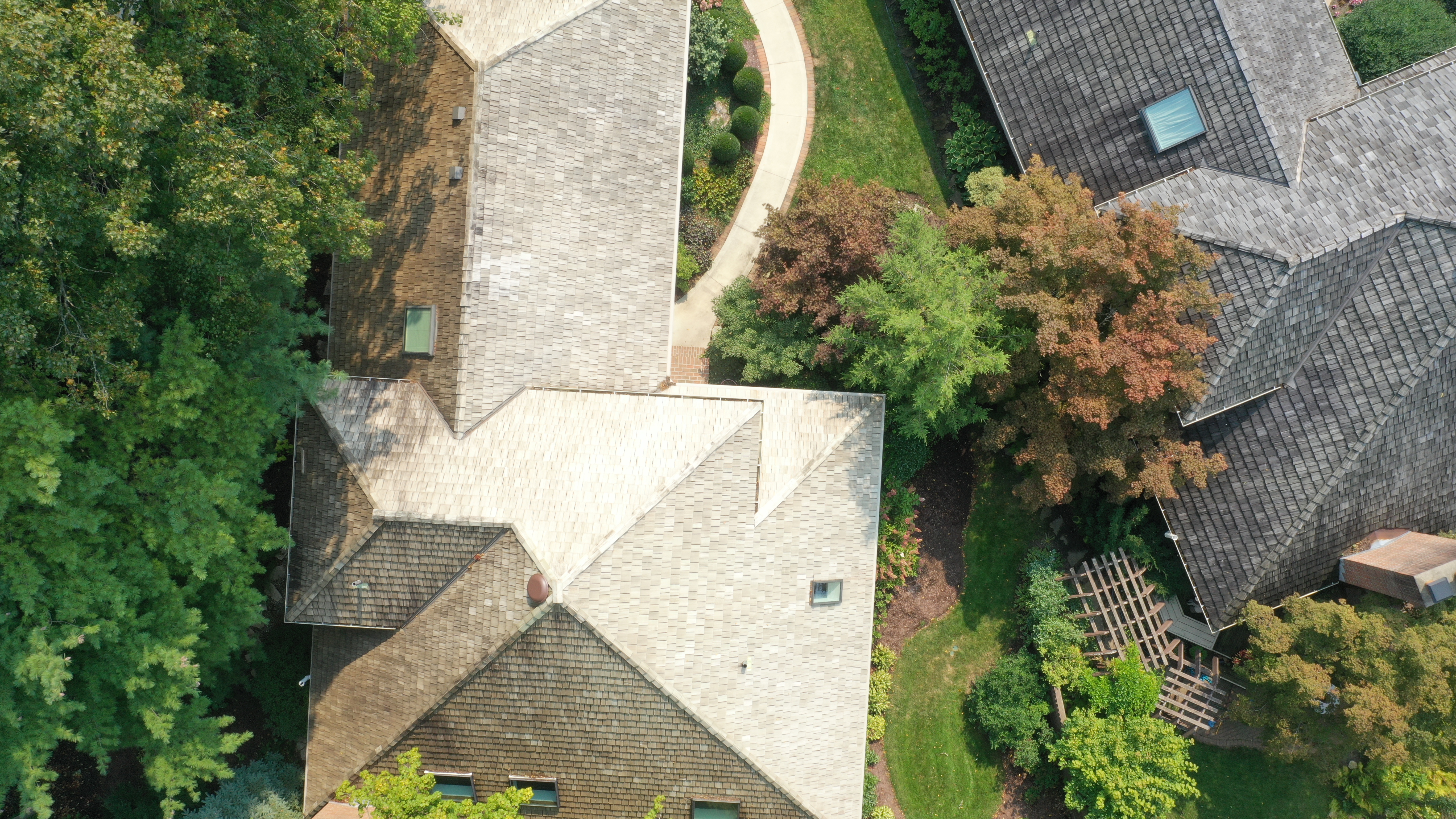 After cedar roof cleaning - golden-tan cedar shakes with neighbor's dark untreated roof visible for dramatic contrast, autumn colors in trees, The Sanctuary Columbus Ohio
