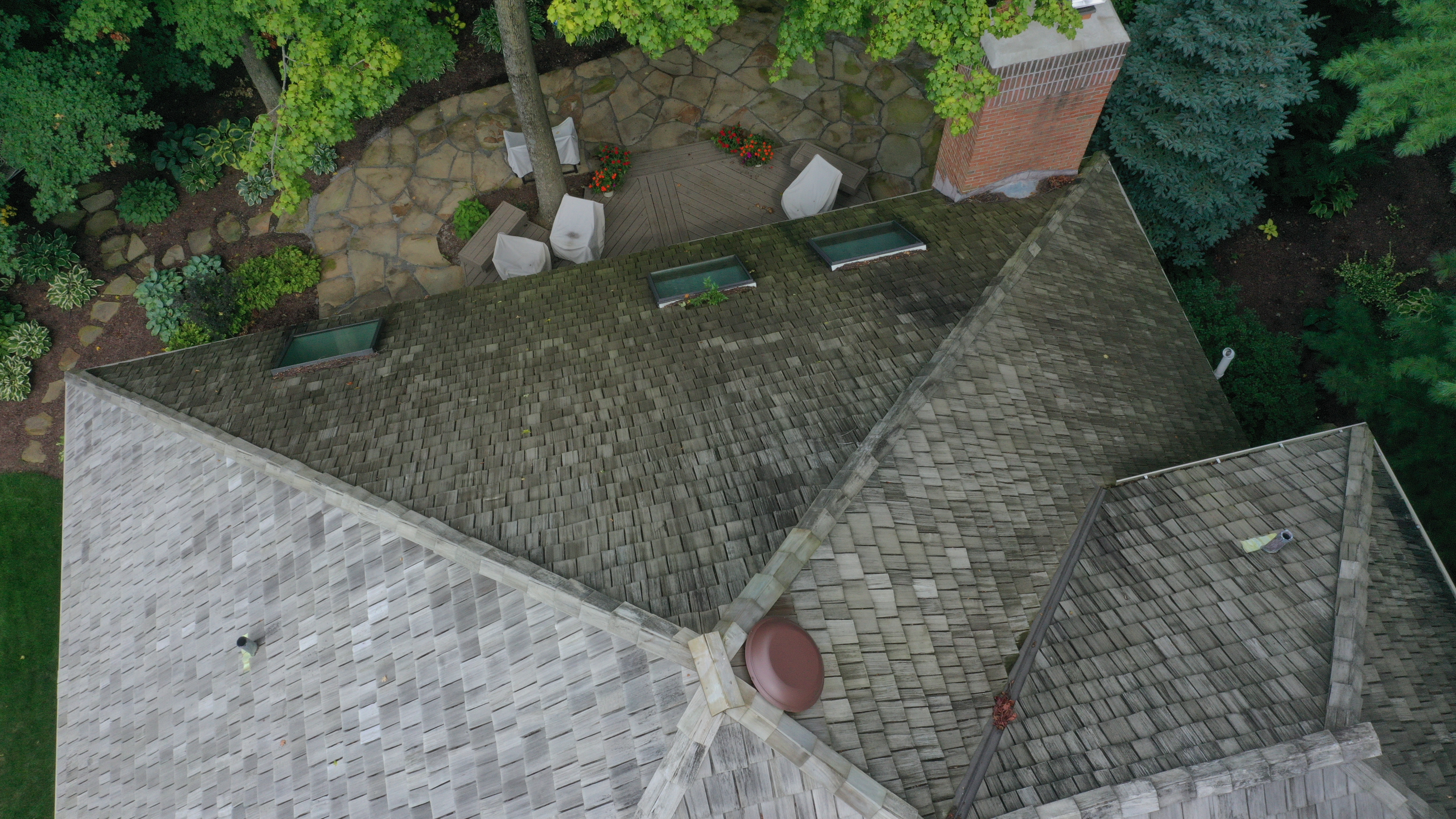 Before cedar roof cleaning - rear view showing skylights, brick chimney, stone patio with covered furniture, dark gray-green cedar shakes, The Sanctuary Columbus Ohio