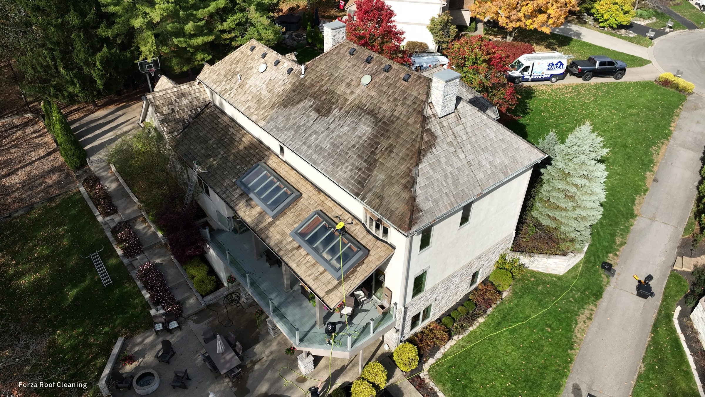 4K drone still showing cedar shake roof near completion of treatment, most of roof lighter, full Muirfield Village property visible with patio and landscaping