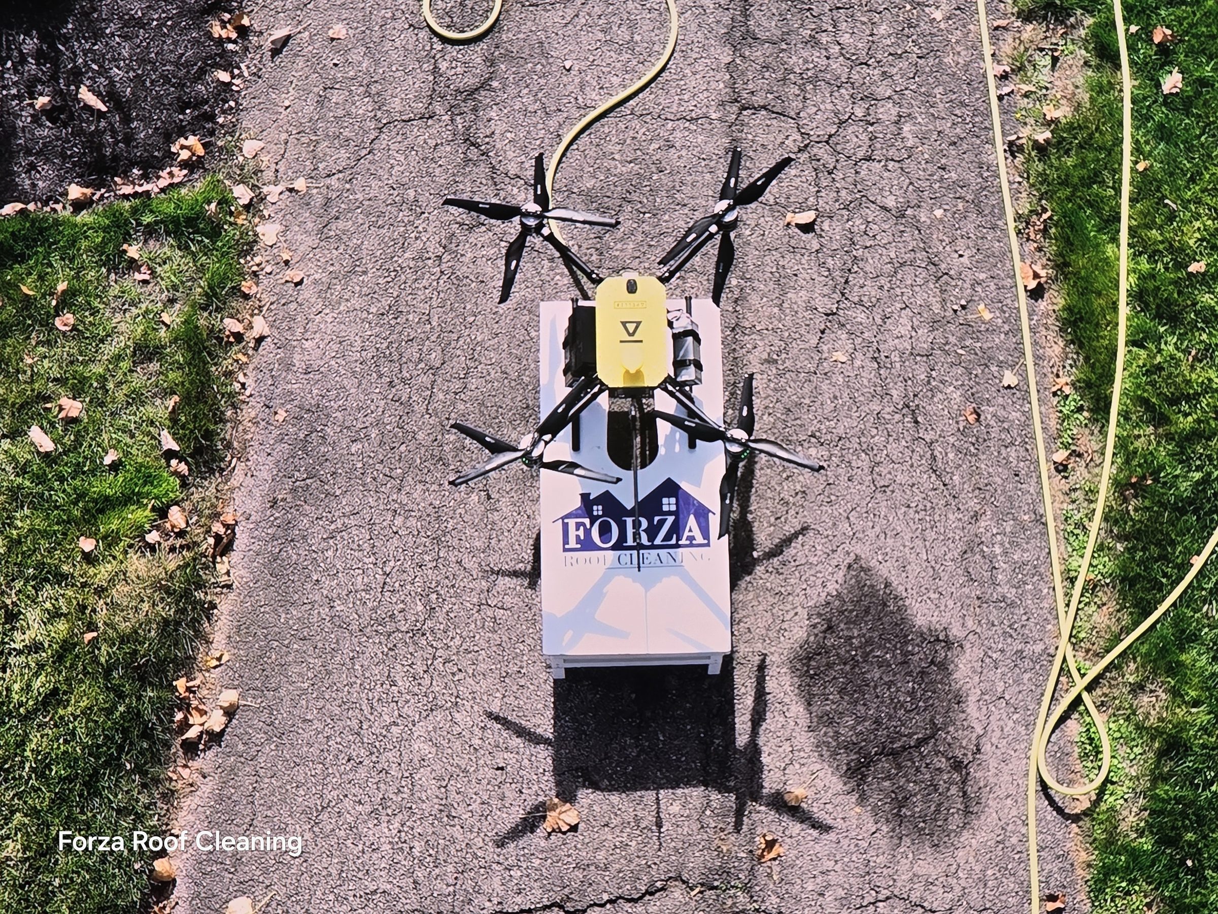 Close-up of Forza Roof Cleaning washing drone on branded landing pad before takeoff, yellow drone body with spray nozzle and hose visible, Muirfield Village Dublin Ohio