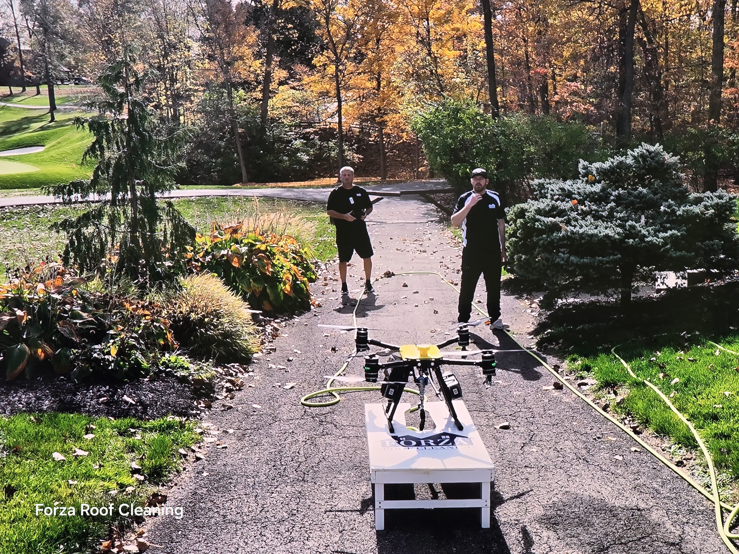 Forza Roof Cleaning crew members standing with washing drone on Forza-branded landing pad in Muirfield Village Dublin Ohio, golf course trees visible